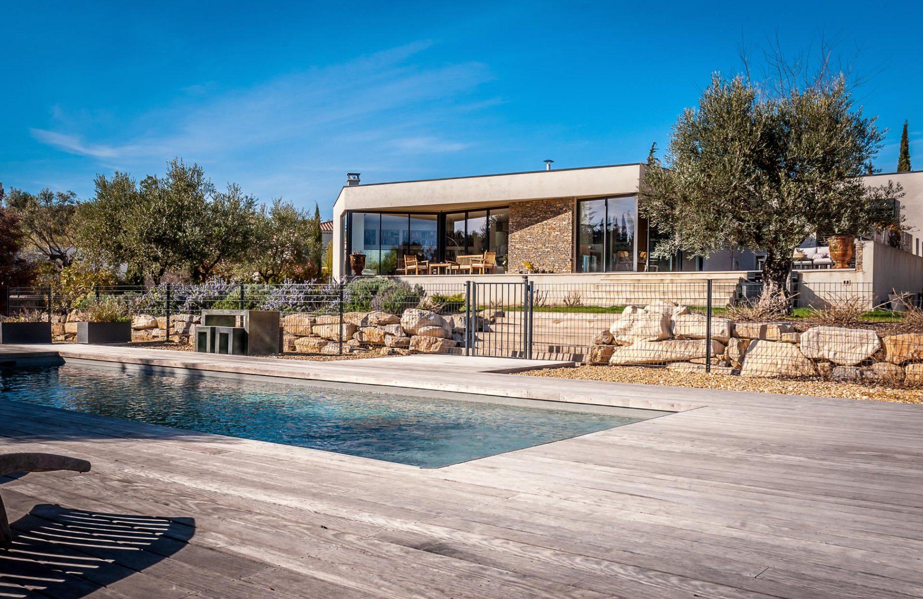 Terrasse en bois autour d’une piscine avec oliviers et maison contemporaine