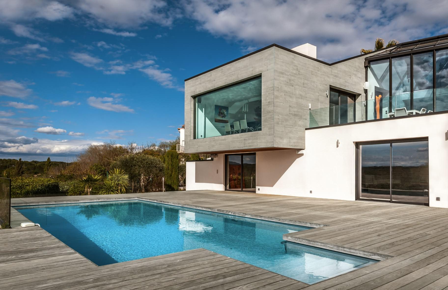 Terrasse en bois autour d’une piscine devant une villa contemporaine