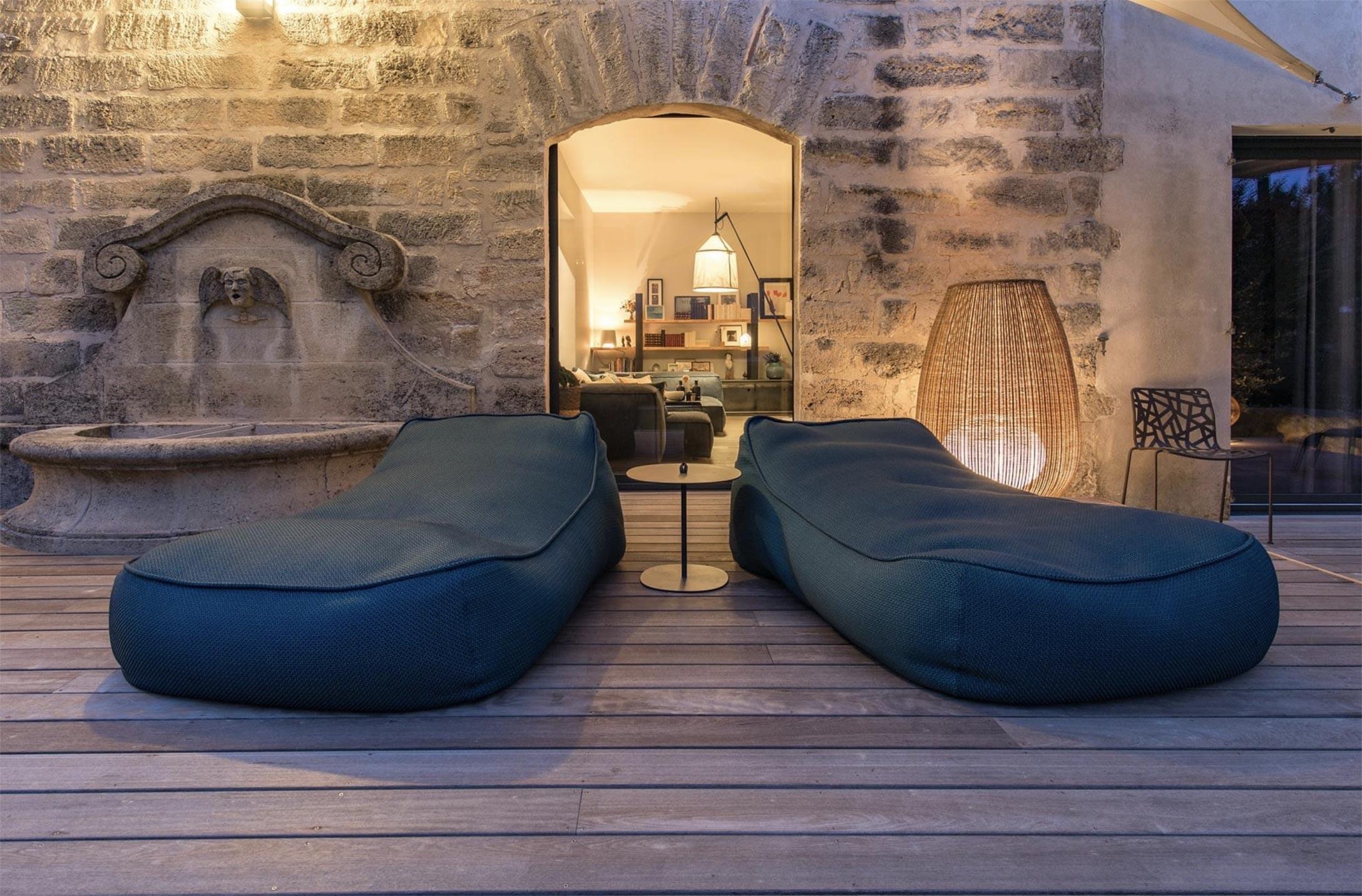 Terrasse en bois avec fauteuils devant une façade en pierre éclairée le soir