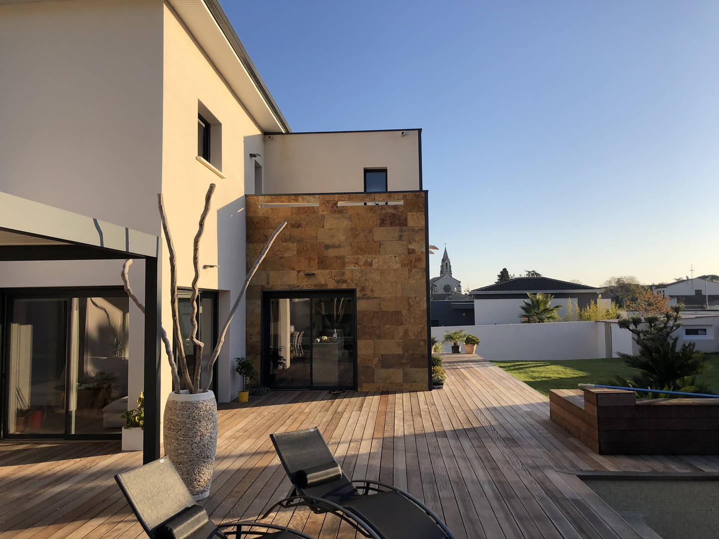 Terrasse en bois au soleil couchant le long d’une maison et de son jardin